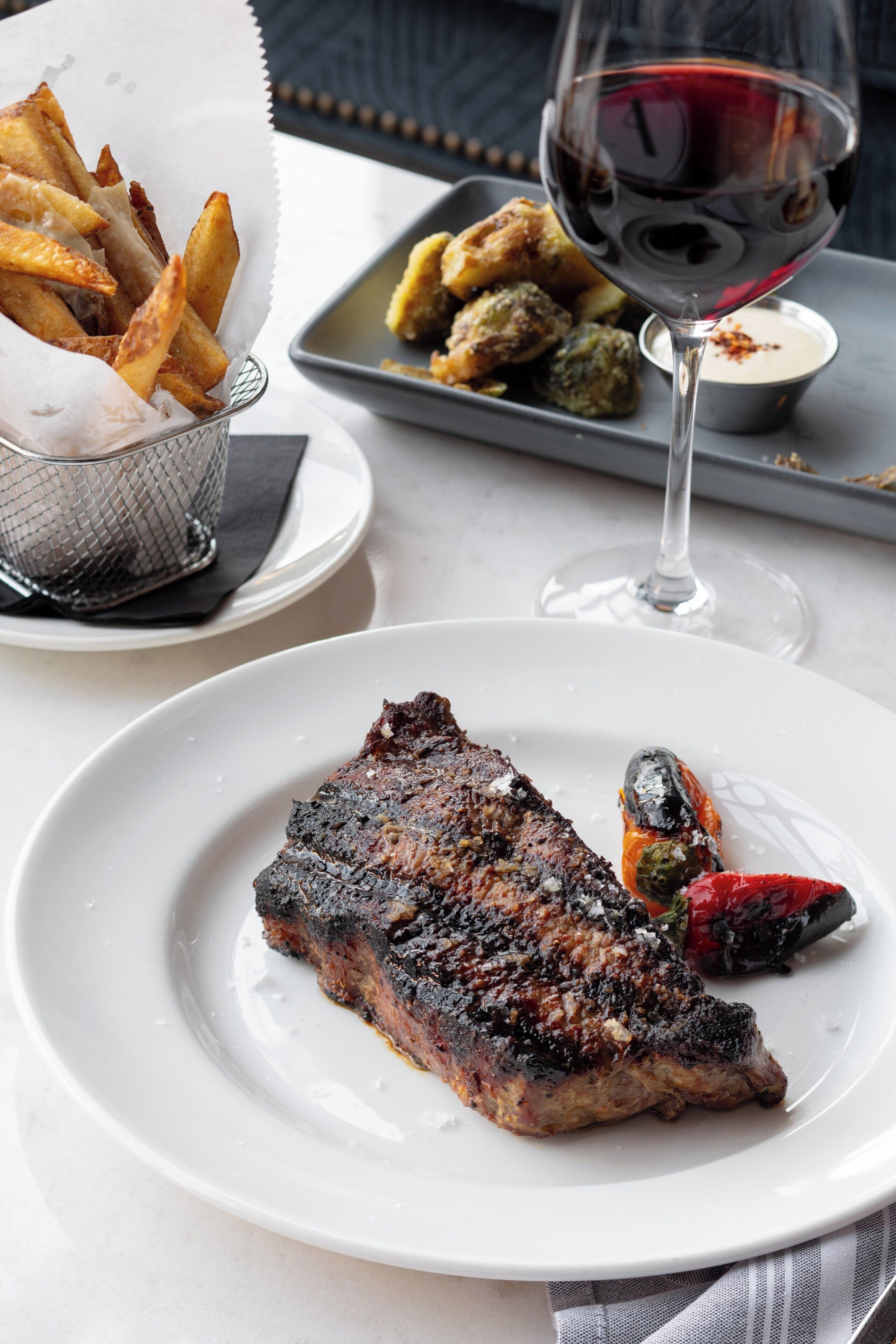 A plate with grilled steak, a glass of red wine, and a basket of fries.