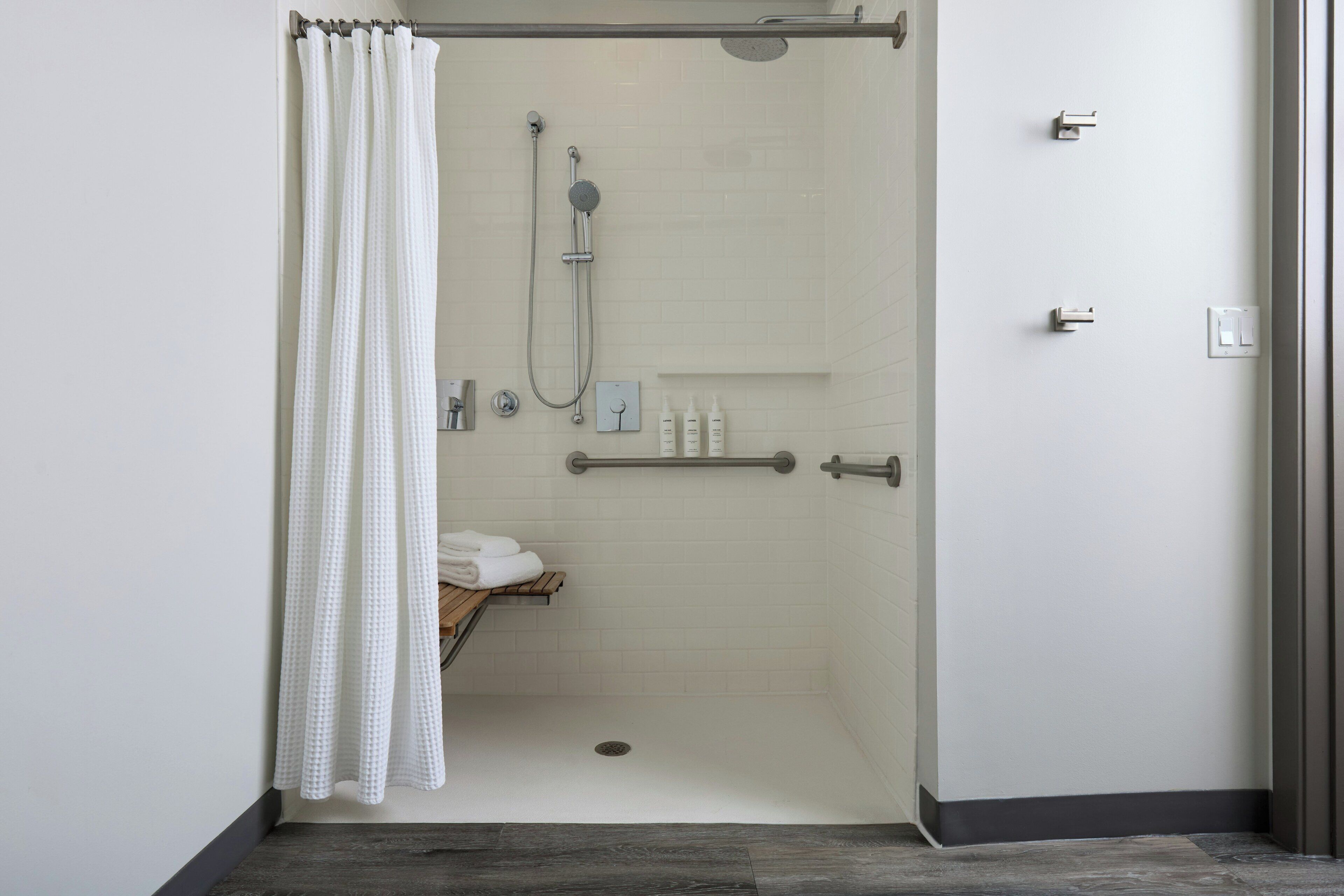 Un área de ducha moderna con puerta de vidrio, alcachofa de ducha, ducha de mano y un perchero para toallas.