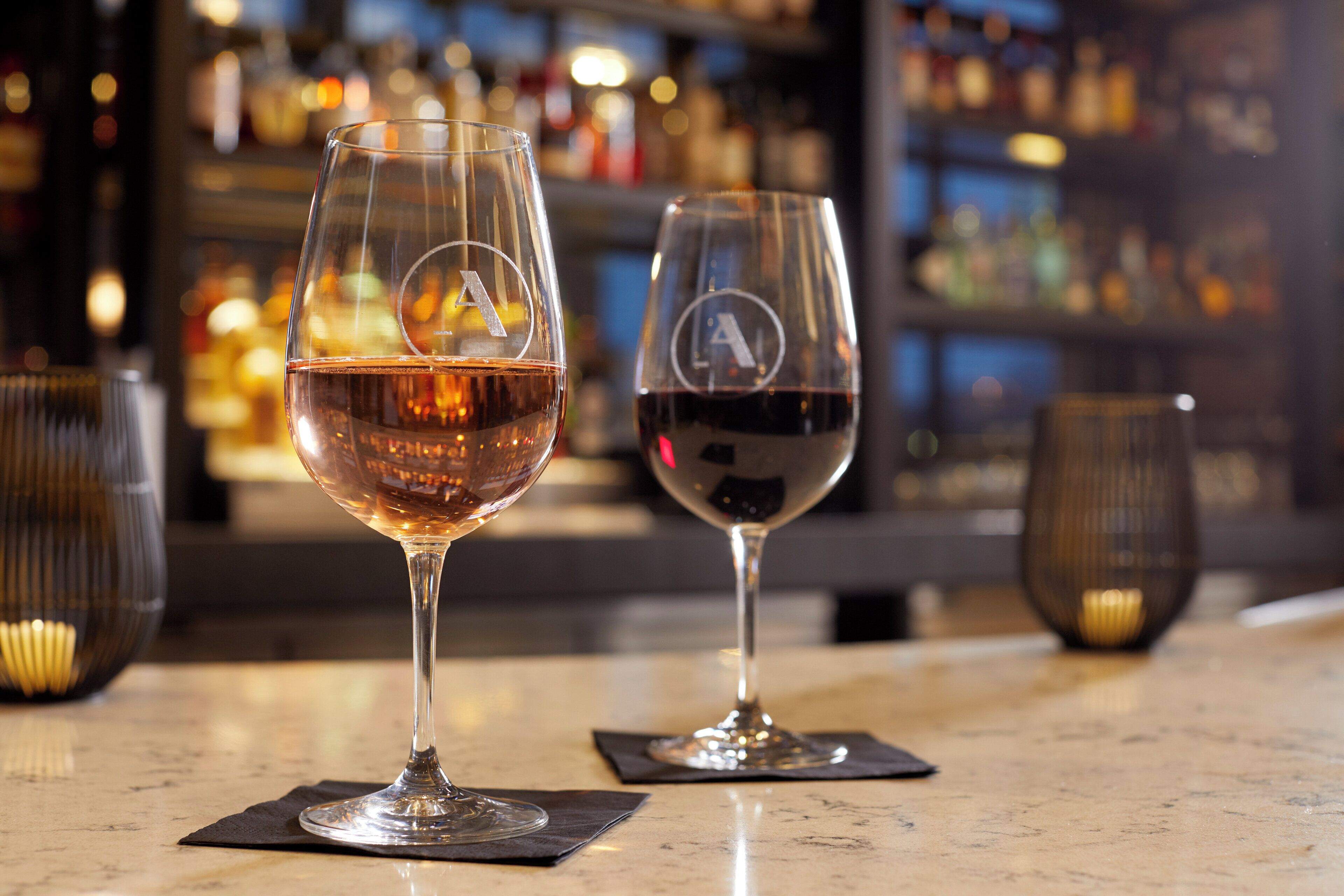 Two wine glasses on a bar counter with a blurred background of shelves and bottles.