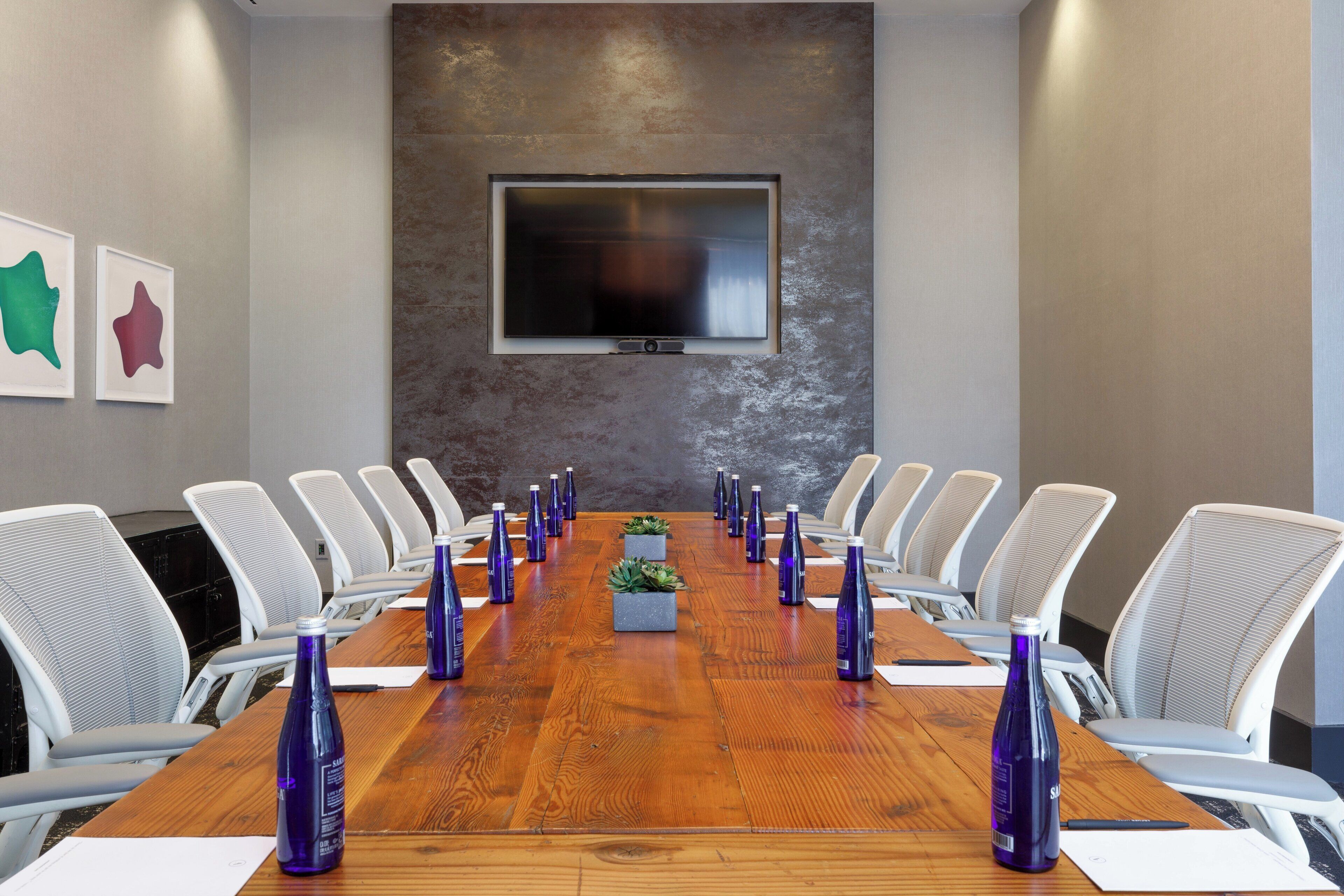 A conference room with a long wooden table, white chairs, and purple water bottles.
