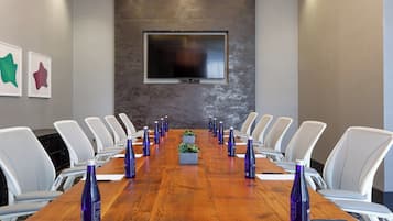 A conference room with a long wooden table, white chairs, and purple water bottles.