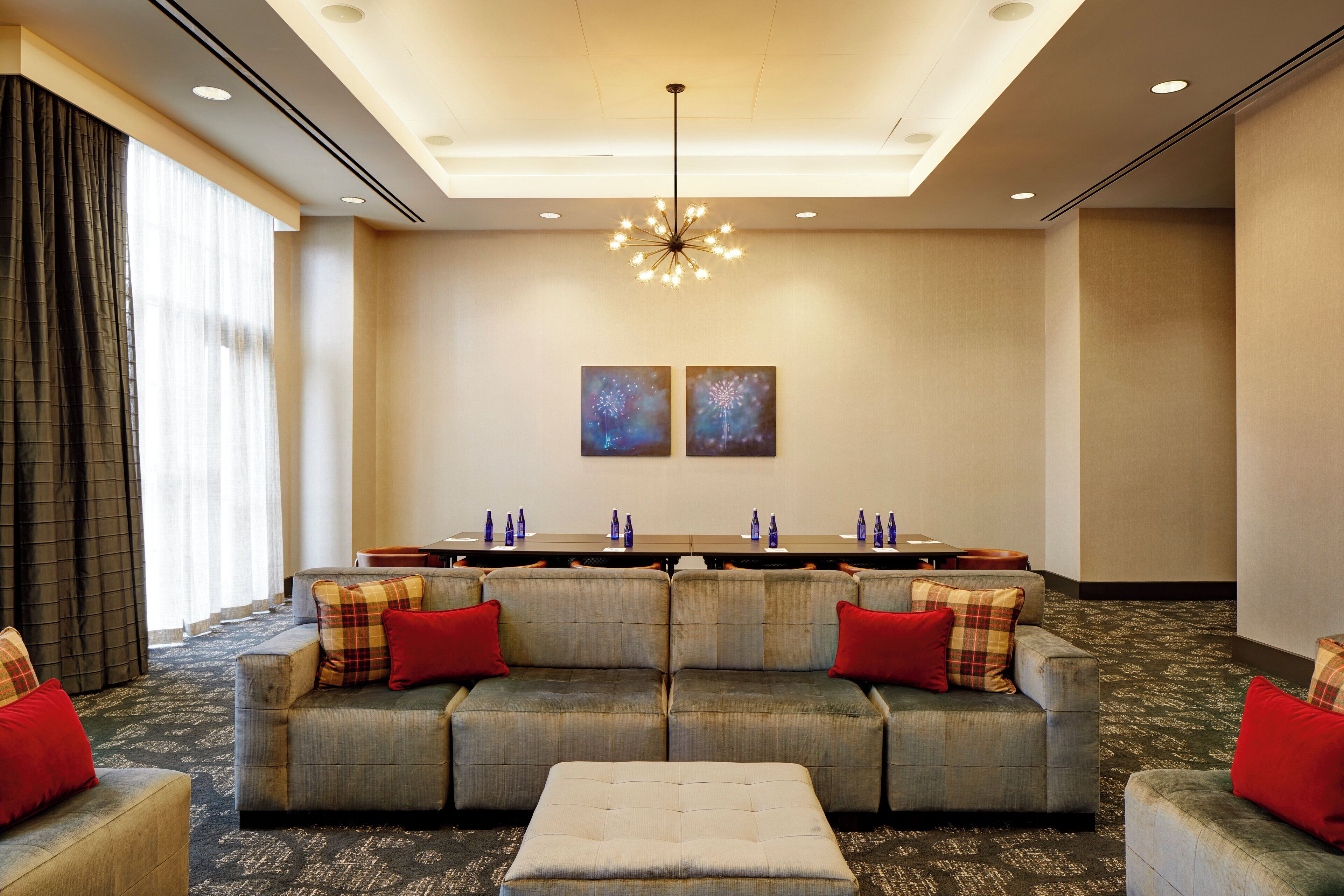 Un moderno vestíbulo de hotel con un sofá modular, un otoman y una mesa larga con botellas azules.