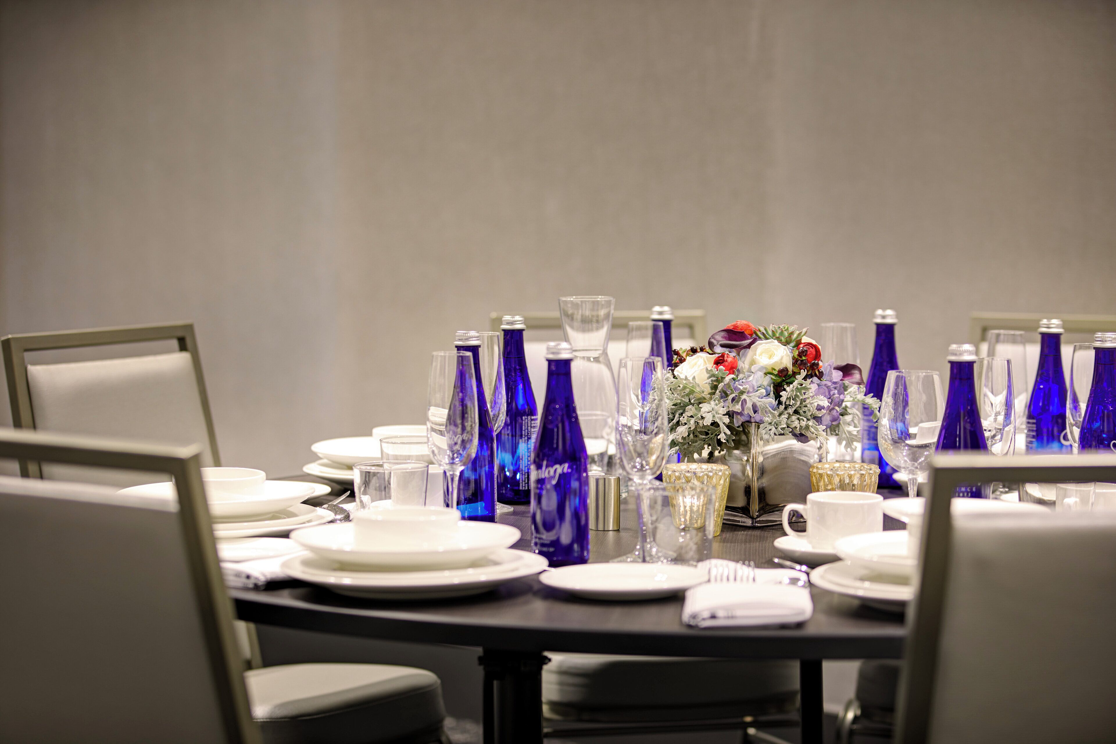 A conference table set with plates, glasses, and blue bottles, surrounded by chairs.