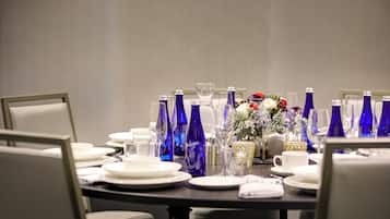 A conference table set with plates, glasses, and blue bottles, surrounded by chairs.