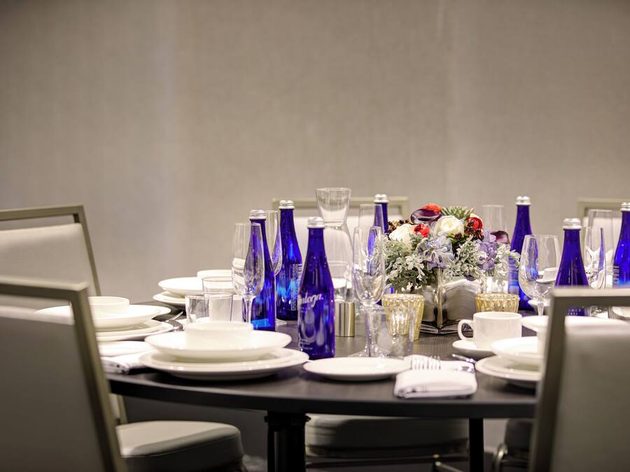 A conference table set with plates, glasses, and blue bottles, surrounded by chairs.