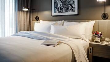 Et hotelværelse med en pænt redt seng, et billede af en zebra i ramme på væggen, og et natbord med en lampe og en vase med blomster.