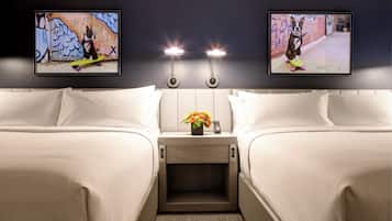 A hotel room with two beds, a nightstand with a vase of flowers, and two framed pictures on the wall.