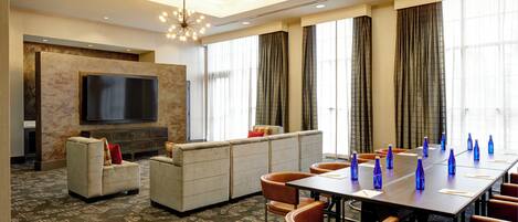 A conference room with a large table, chairs, a sofa, and a TV.