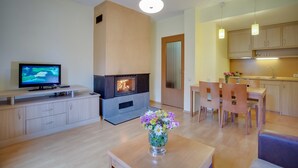 A modern living room with a fireplace, a television, a dining area, and a kitchen. - Malina Residence Hotel (Smolyan)