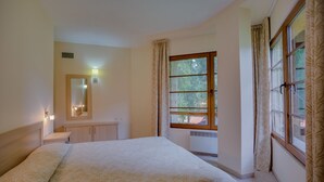 A hotel room with a large bed, a bedside table, a mirror, a window with curtains, and a view of trees outside. - Malina Residence Hotel (Smolyan)