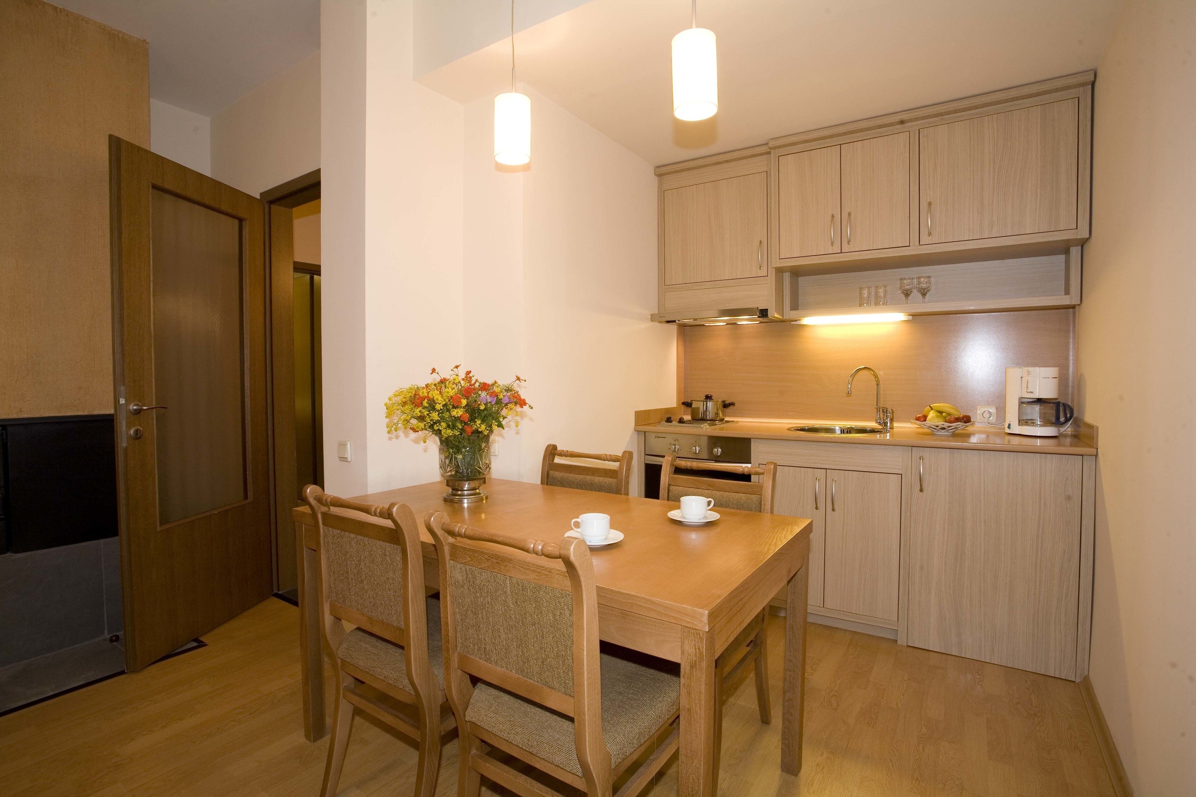 A compact kitchen with wooden cabinets, a dining table with chairs, and pendant lighting.