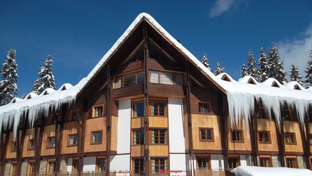 A wooden lodge with a steeply pitched roof, large windows, and a snow-covered landscape. - Malina Residence Hotel (Smolyan)
