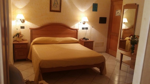 A neatly arranged bedroom with a wooden bed, bedside lamps, a nightstand, a mirror, and a small table with a vase of flowers. - Hotel Mistef (Falerna)