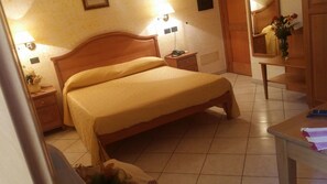 A bedroom with a large bed, bedside lamps, a nightstand, a wooden dresser, and a small table with a vase of flowers. - Hotel Mistef (Falerna)