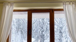 A room with a bed, a window with curtains, and a view of snow-covered trees. - Apart Hotel The Castle (Smolyan)