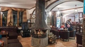 A cozy interior with a central wood-burning stove, comfortable seating, and a bar area. - Apart Hotel The Castle (Smolyan)