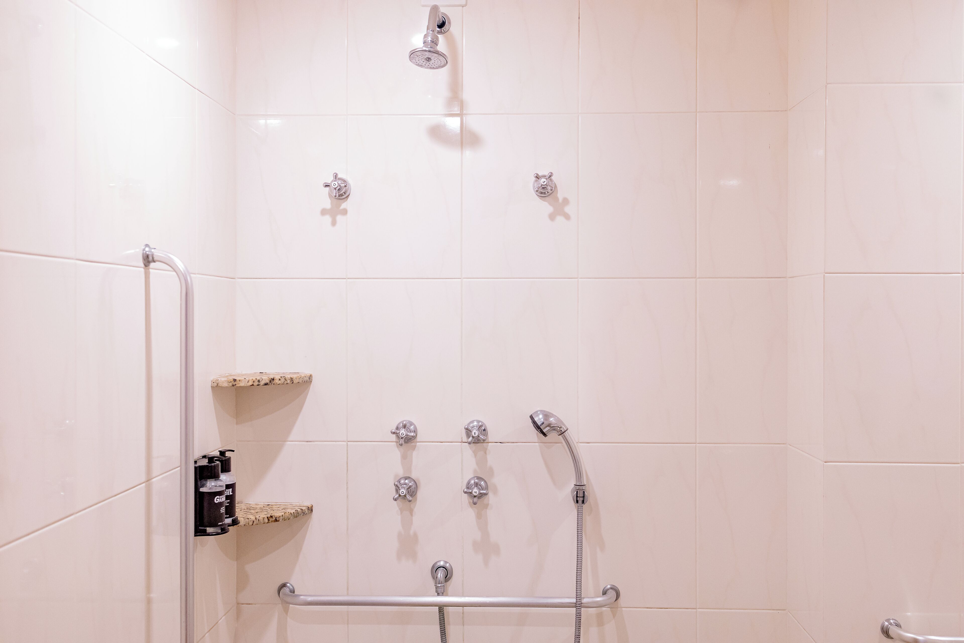 A shower with multiple heads and a grab bar.