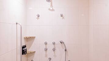A shower with multiple heads and a grab bar.
