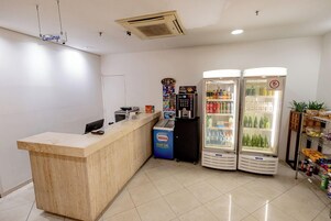 Un área de recepción con un mostrador de madera, una máquina expendedora de Nestlé y dos refrigeradores para bebidas.