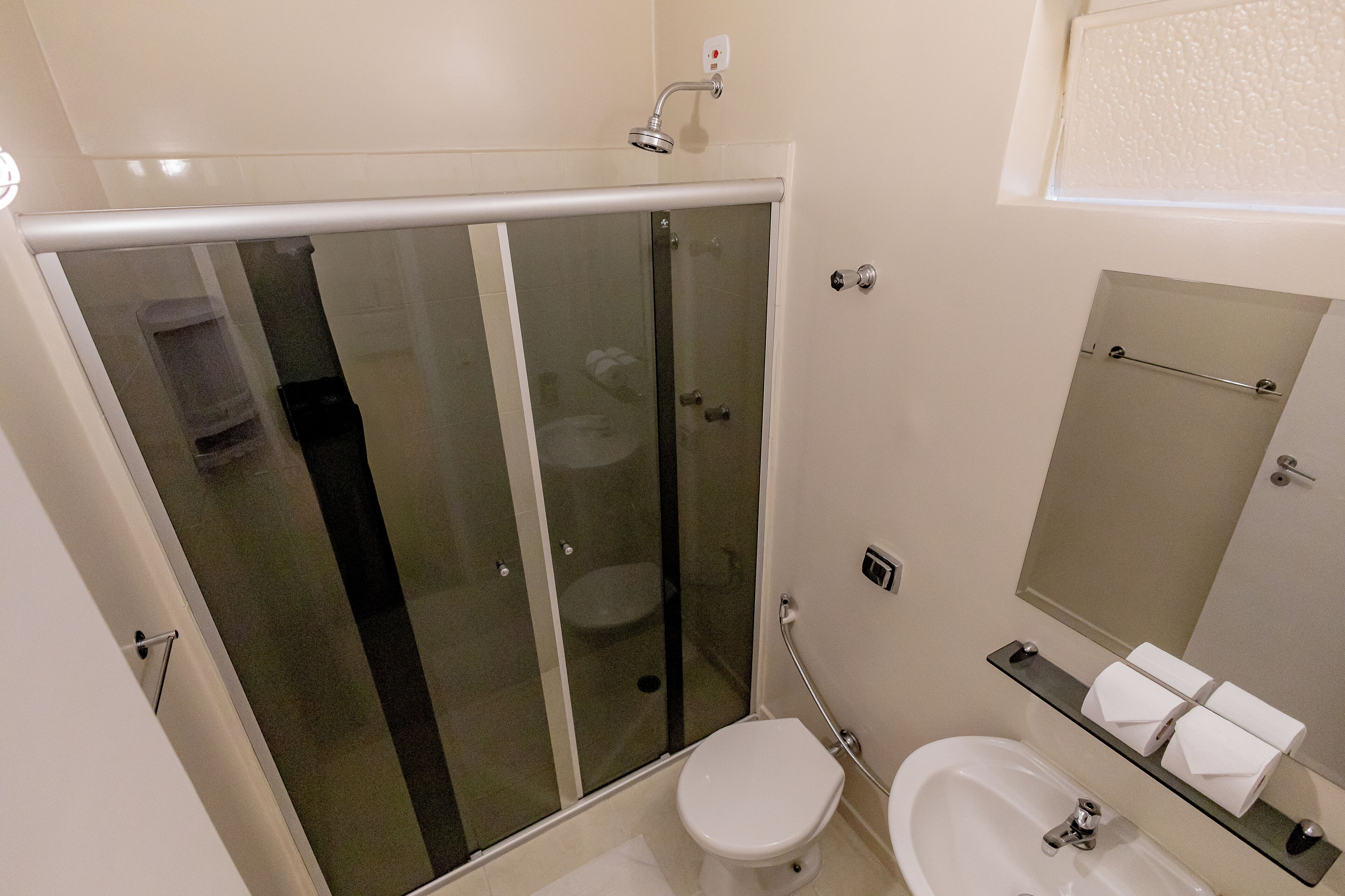 A modern bathroom with a glass-enclosed shower, a toilet, a bidet, and a sink with a mirror above it.