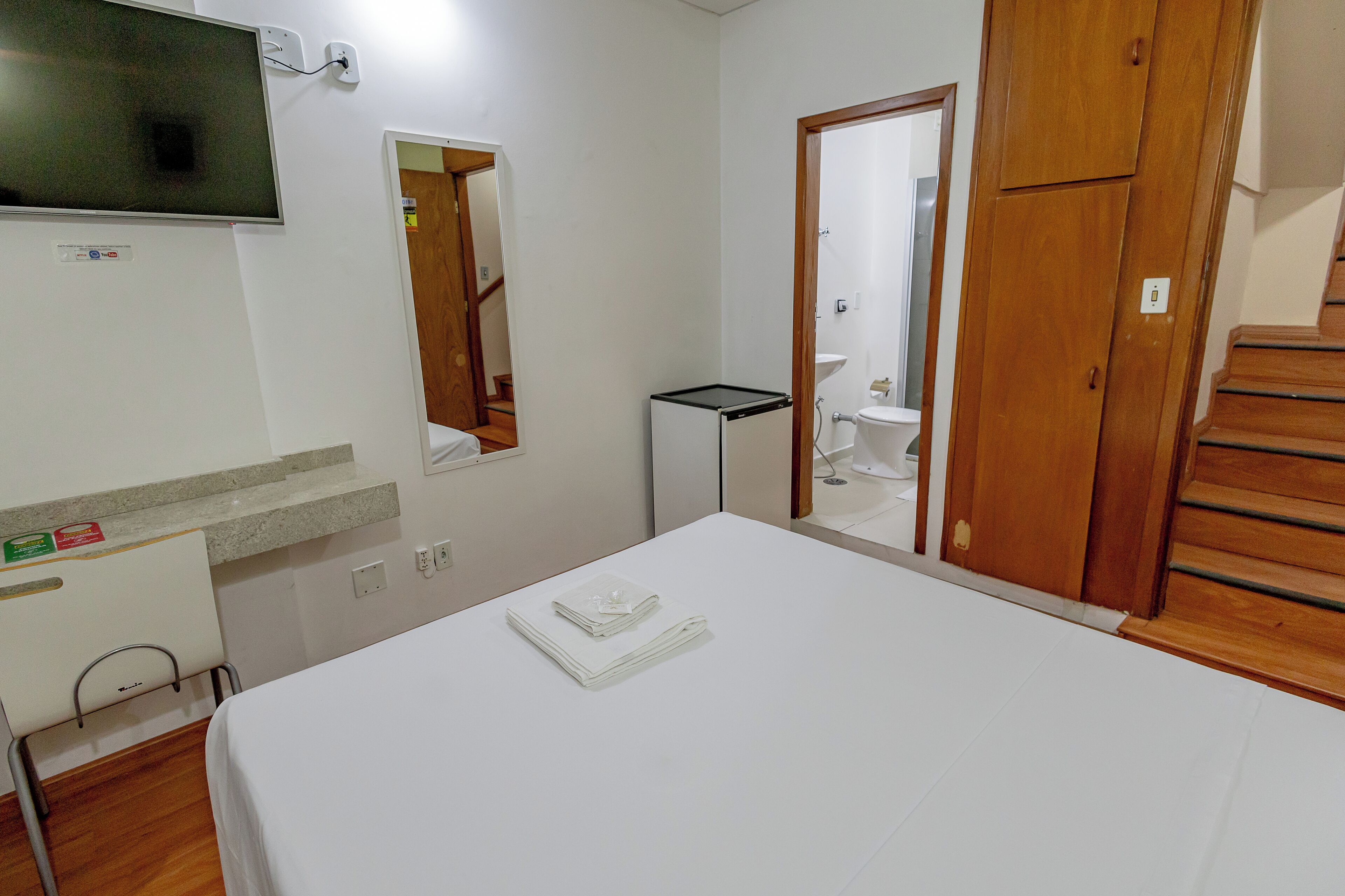 Een hotelkamer met een bed, een aan de muur bevestigde televisie, een klein nachtkastje en een houten garderobe.