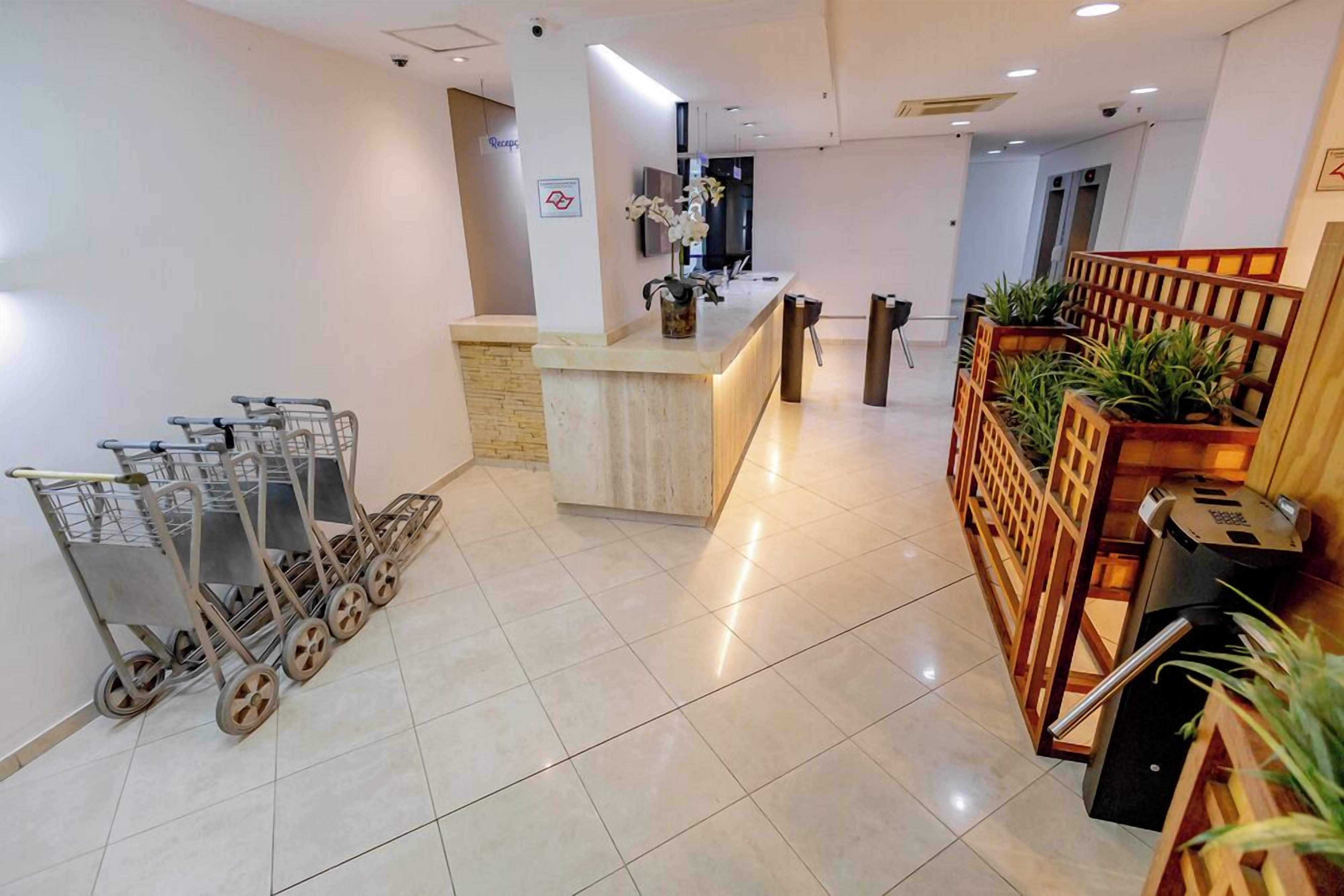 A hotel reception area with a counter, several shopping carts, and a seating area with plants.