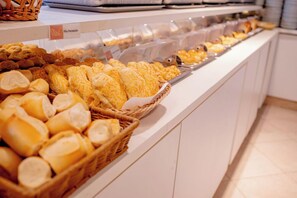 A buffet with various baked goods, including bread and pastries, displayed in baskets and trays. - Hotel San Gabriel (São Paulo)
