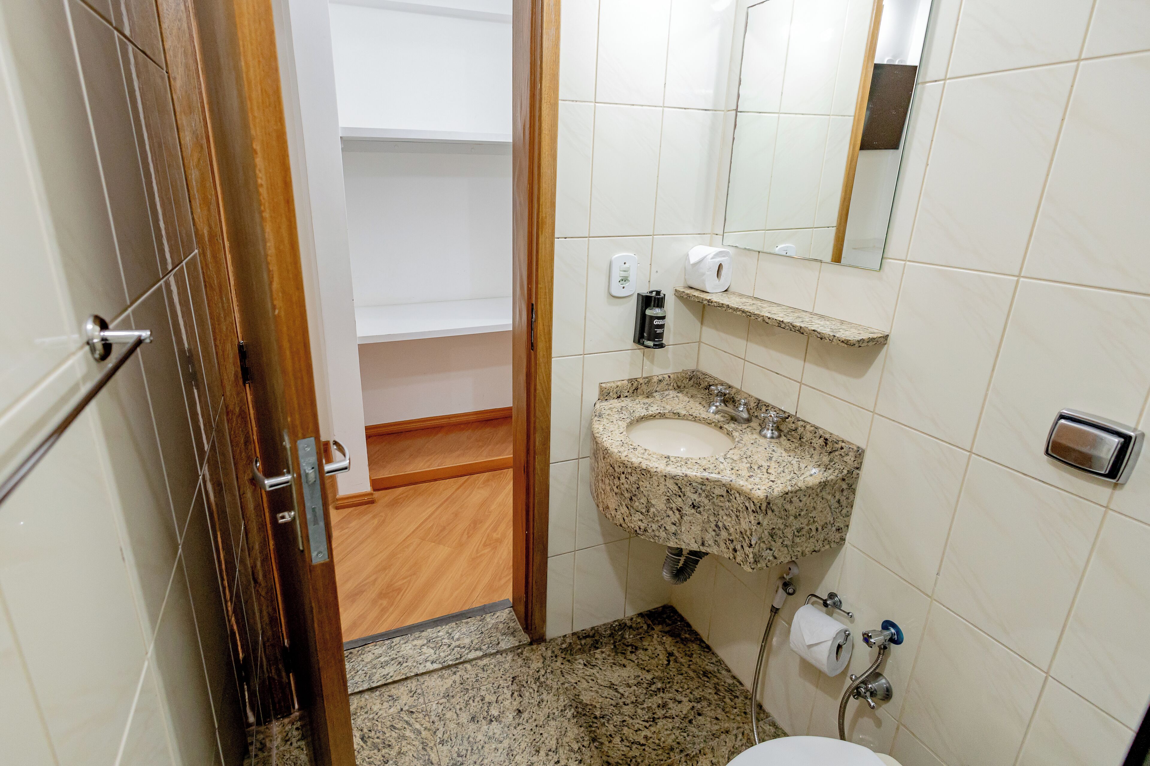 A bathroom with a granite sink, a toilet, a mirror, and a shelf with toiletries.