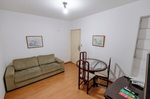 A living room with a sofa, a glass-top table with chairs, a door, and two framed pictures on the walls.