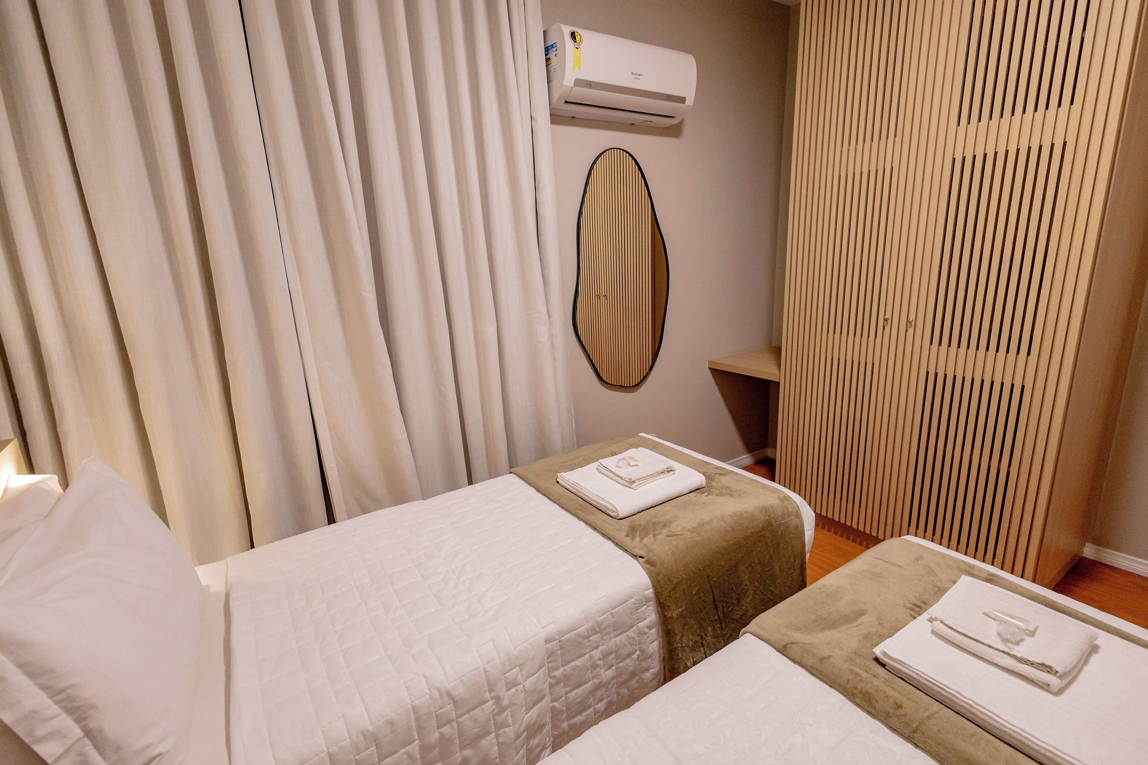 Une chambre d’hôtel avec deux lits, un climatiseur fixé au mur et un rideau.