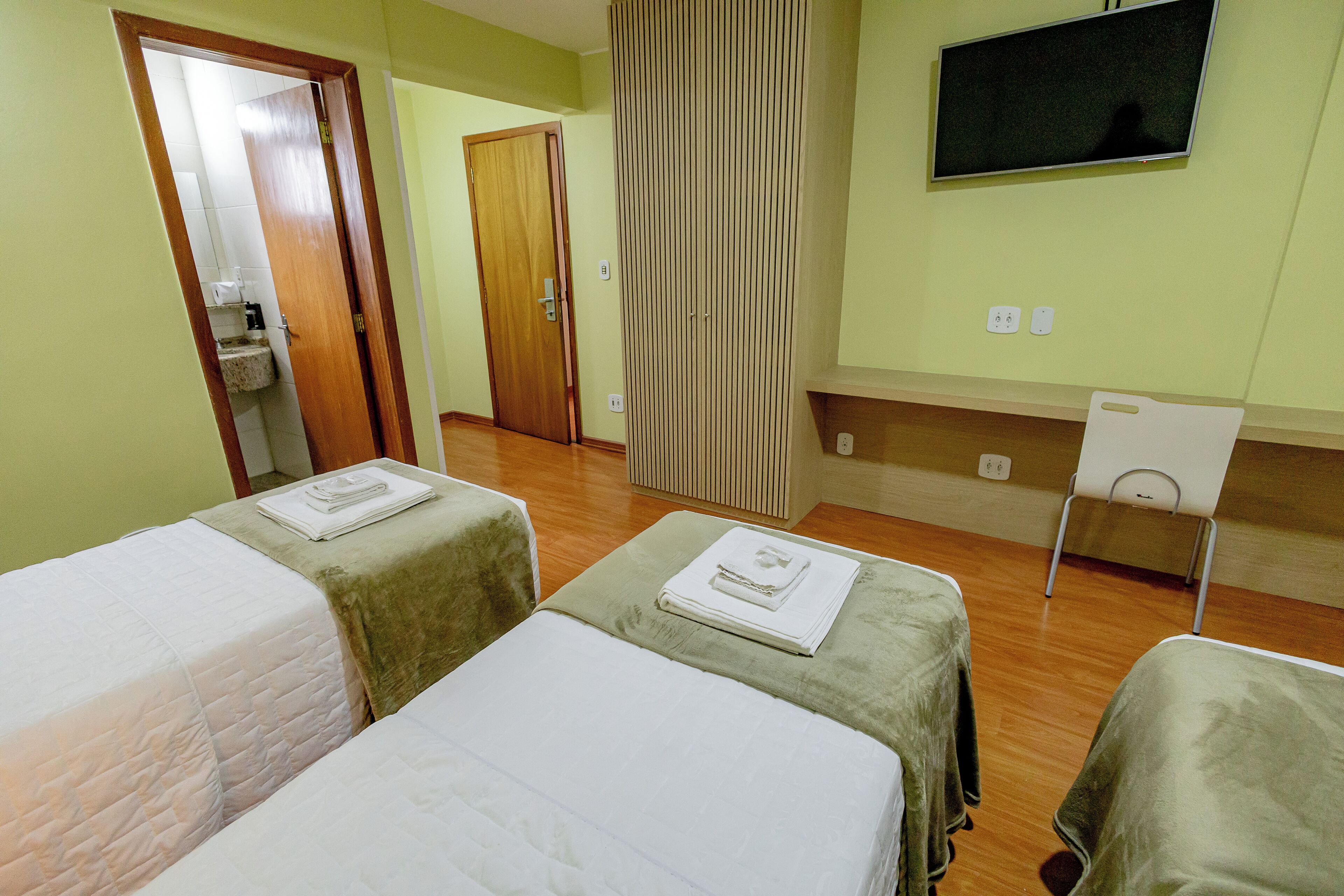 Habitació d'hotel amb dos llits, televisió i un bany visible a través d'una porta oberta.