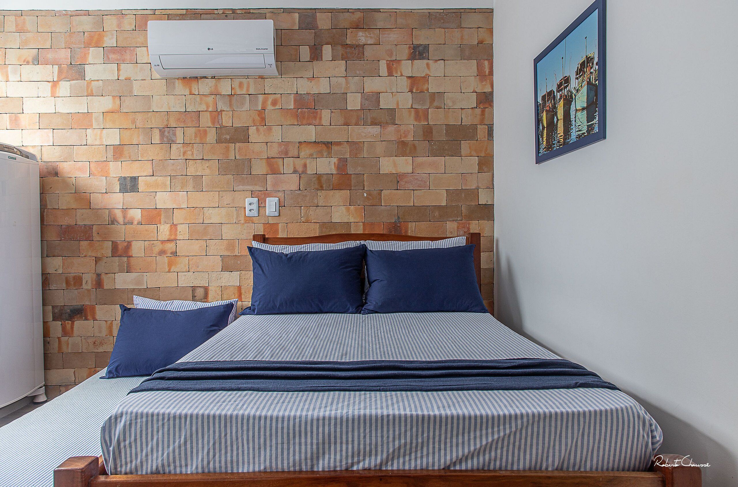 Una camera da letto con parete in mattoni, un letto con biancheria a righe e un quadro appeso al muro.
