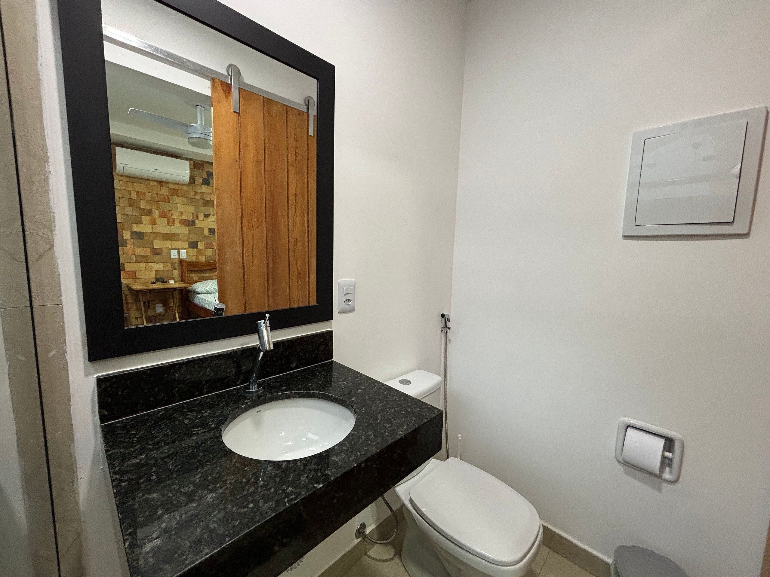 Un baño con un lavabo de mármol negro, un inodoro blanco y un espejo con marco de madera.