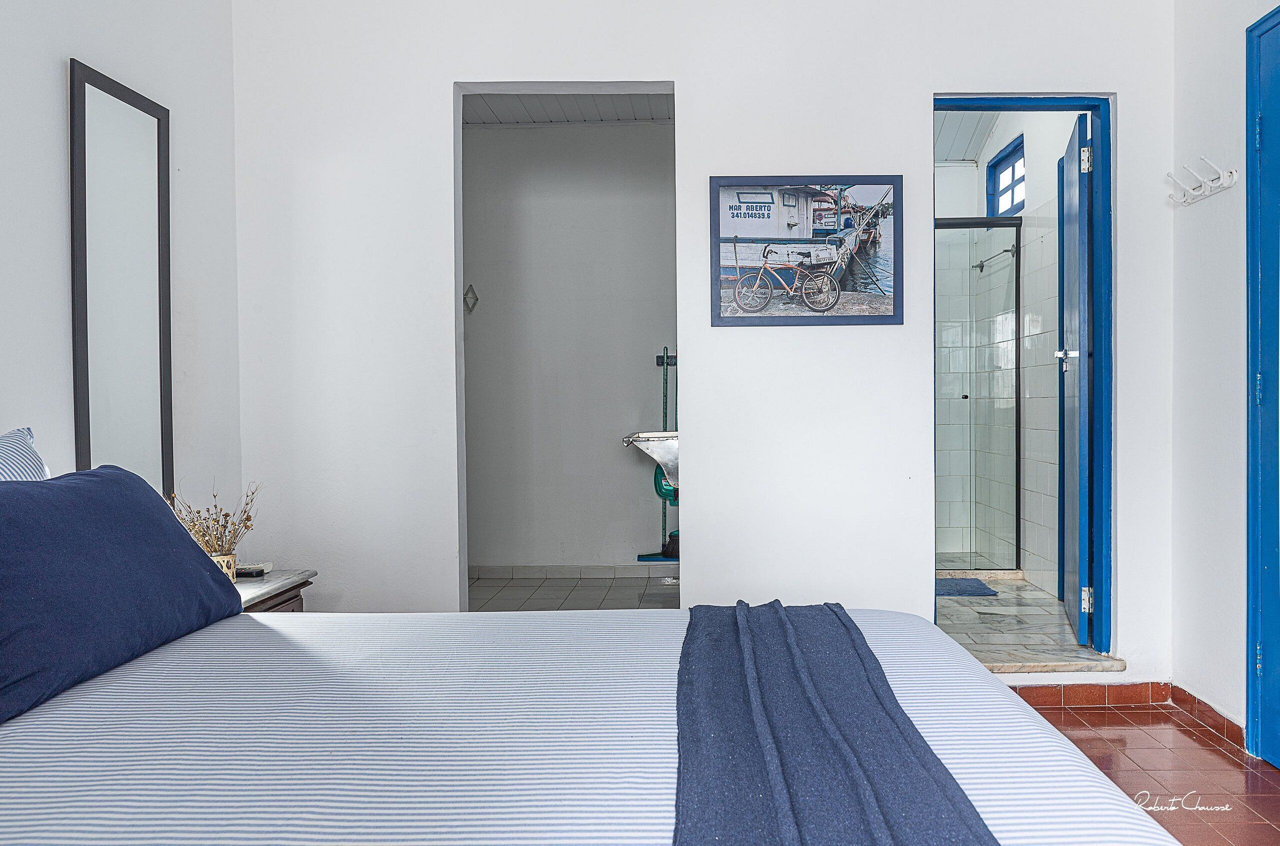 Une chambre à coucher avec un lit, une table de chevet, un tableau encadré et une porte de salle de bain visible à travers une porte entrouverte.