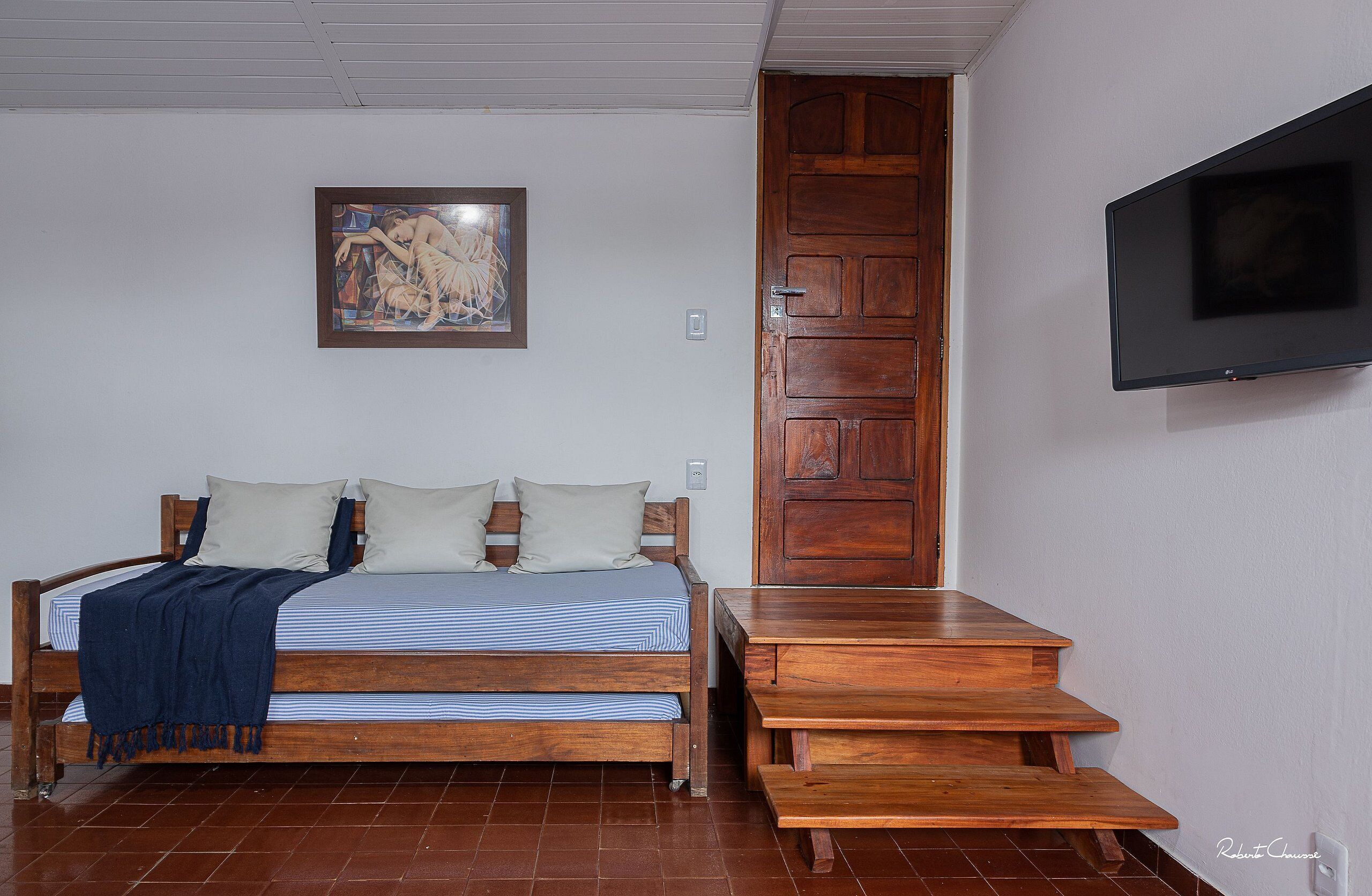 A bedroom with a bed, a wooden door, a TV mounted on the wall, and a painting on the wall.