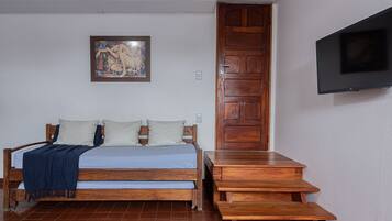 A bedroom with a bed, a wooden door, a TV mounted on the wall, and a painting on the wall.