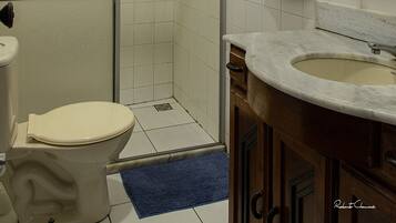 A bathroom with a toilet, shower, sink, and a towel hanging on the wall.