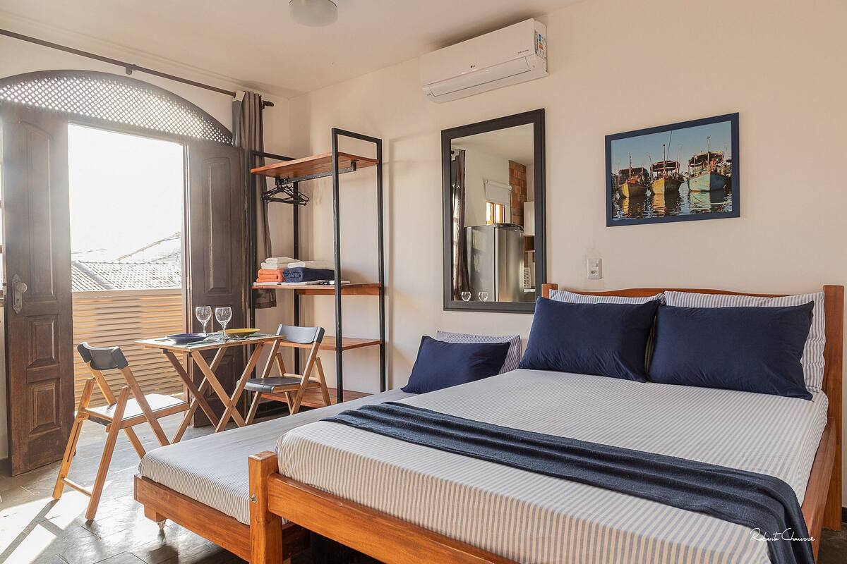 Ein Schlafzimmer mit Bett, Schreibtisch und Stuhl. Es gibt ein Fenster, einen Spiegel und ein Bild an der Wand.