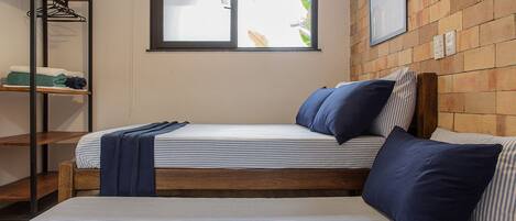 A room with two beds, a window, a wall-mounted picture, and a shelf with folded clothes.