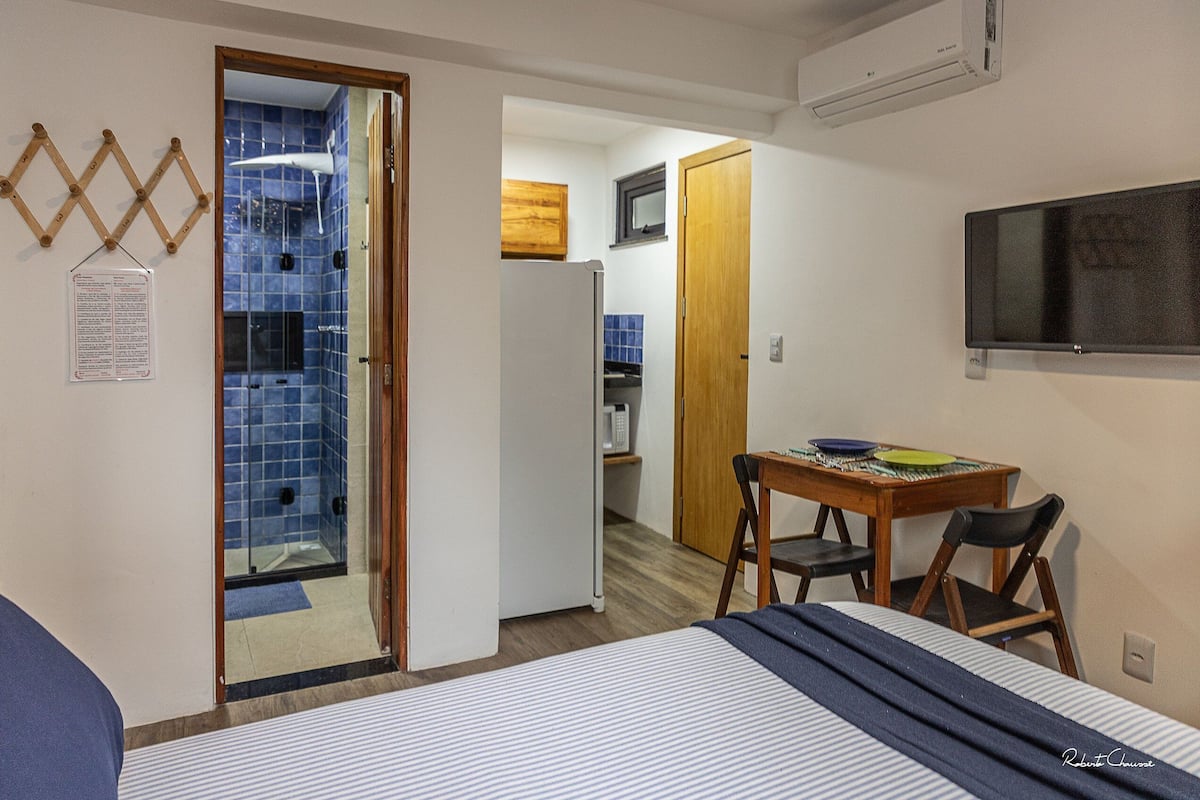 Ein kleines Hotelzimmer mit Bett, Tisch mit Stühlen, einer Küchenzeile und einem Badezimmer mit Duschkabine.