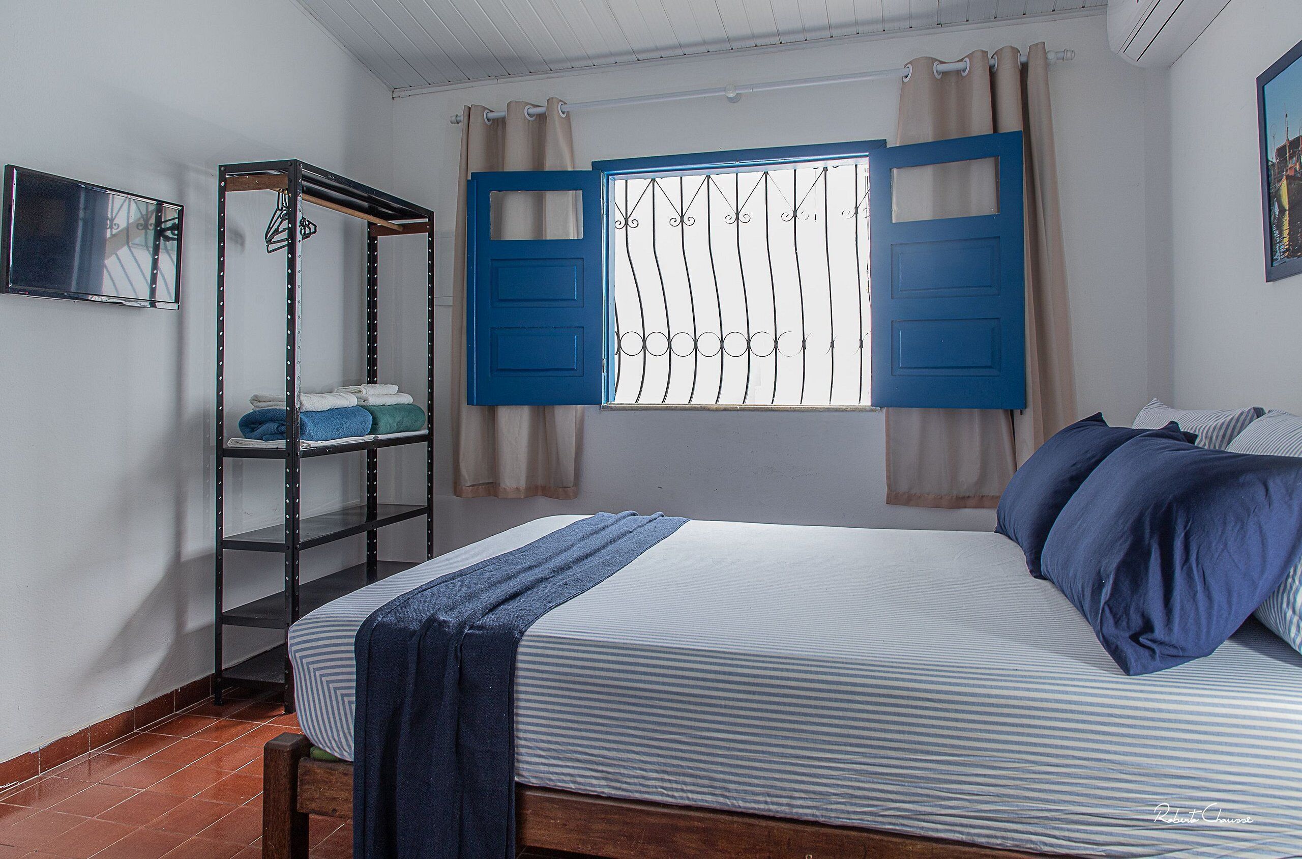 A bedroom with a bed, a metal shelf unit, and a window with blue shutters.