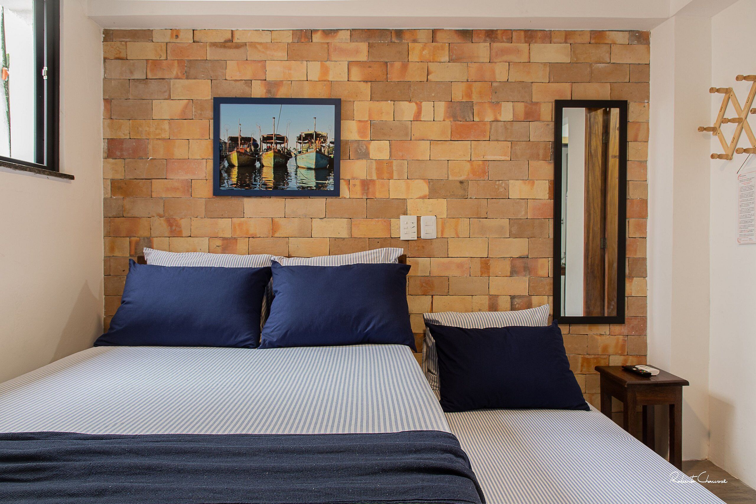 A bedroom with a brick-patterned headboard, a bed with striped bedding, and a framed picture of boats on the wall.