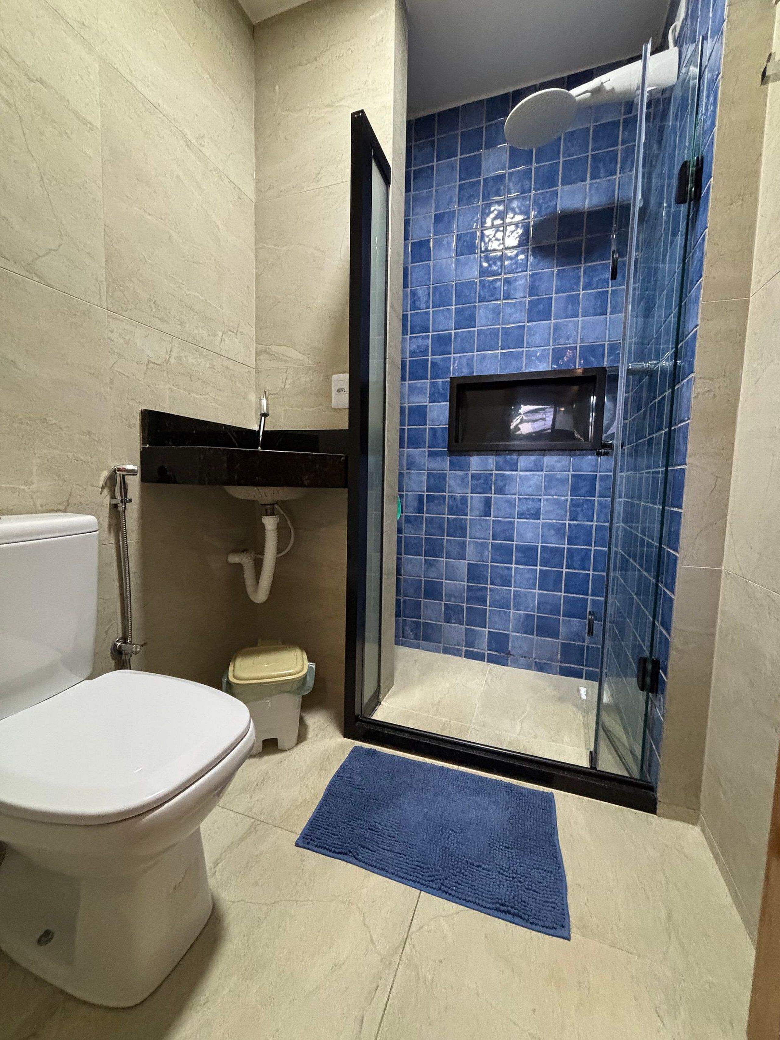 A bathroom with a toilet, a sink, and a glass-enclosed shower area with blue tiles.
