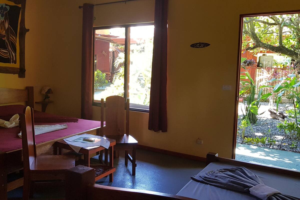 Quarto com cama, escrivaninha e cadeira. Janela com vista para um jardim.