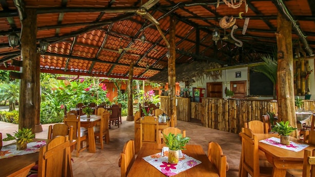 Un restaurante al aire libre con mesas y sillas de madera, rodeado de abundante vegetación.