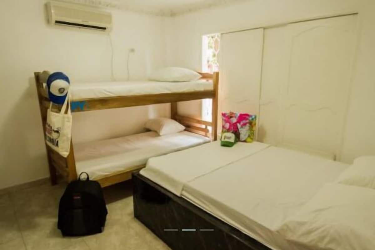 A small, single-room accommodation with a bunk bed, a single bed, a suitcase, and a bag of snacks.