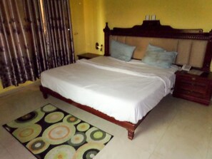 A bedroom with a bed, a nightstand, a wooden headboard, and a patterned rug. - Golden Bird Hotel & Suites (Lekki)
