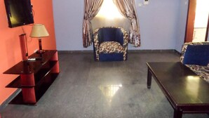 A living room with a sofa, a TV, a lamp, and a chair. - Golden Bird Hotel & Suites (Lekki)
