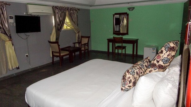 A hotel room with a bed, a desk, a chair, a television, and a window with curtains. - Golden Bird Hotel & Suites (Lekki)