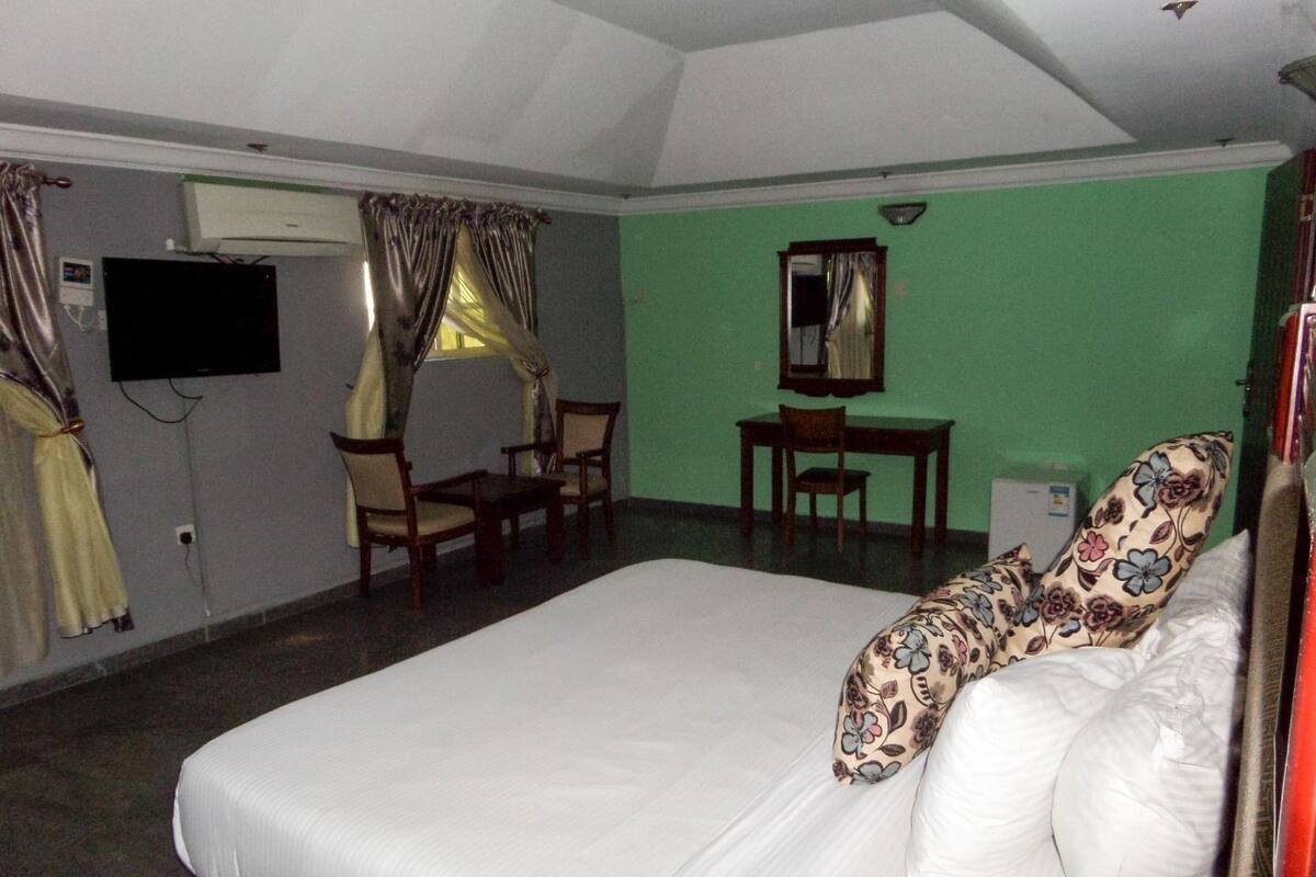 A hotel room with a bed, a desk, a chair, a television, and a window with curtains.